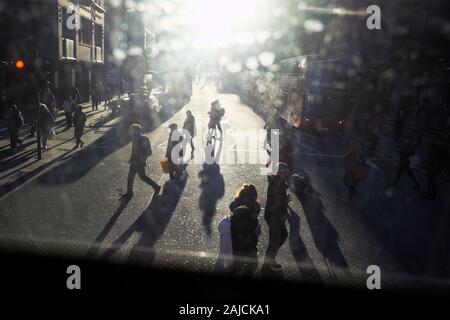 View of pedestrians crossing a road in London looking into the glare of the sun from the top floor of a double decker bus East London UK  KATHY DEWITT Stock Photo