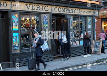 Verde & Company shop at Christmas time & woman tourist walking looking at mobile cell phone with luggage in Spitalfields East London UK KATHY DEWITT Stock Photo