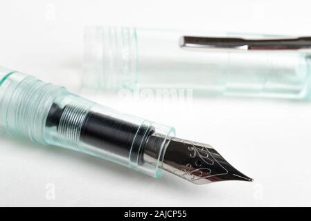 A close-up shot with selective focus of a green glass demonstrator fountain pen set on a plain white background. Stock Photo