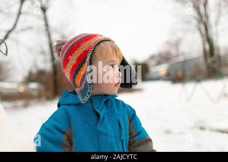 Side view portrait of toddler boy wearing knit hat outdoors in snow Stock Photo