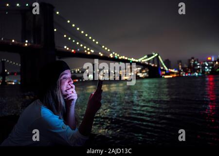 Attractive woman using her smartphone at night on the Brooklyn Bridge Stock Photo
