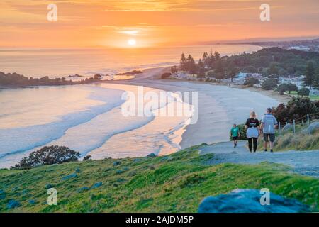Mount Maunganui New Zealand - December 14 2019; Early morning walkers at sunrise on track on slopes Mount Maunganui eastward view along ocean beach