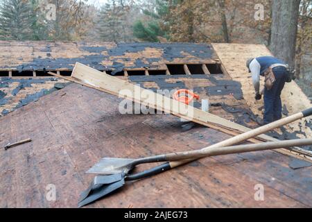 Tools on a rooftop are ready for workers to use, as a man finishes preparing the area for new shingles Stock Photo