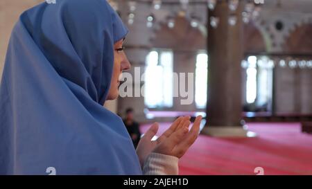 thoughtful woman in blue headscarf prays holding hand palms up standing in ancient mosque extreme close-up Stock Photo