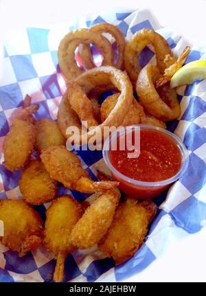 Basket of crispy fried shrimp with breaded onion rings and a red cocktail sauce Stock Photo