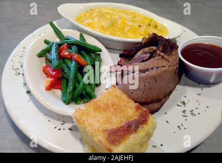 Tender slices of smoked brisket, is served with green beans and red pepper, creamy mac and cheese, a cup of spicy barbecue sauce and a square of savor Stock Photo