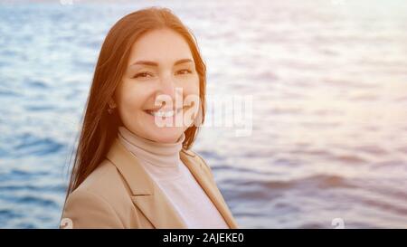 beautiful woman looks ahead and smiles posing against impressive nature and sea waves close-up Stock Photo
