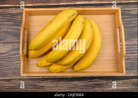 Bunch of ripe yellow bananas on a wooden tray on a wooden background. Close up Stock Photo