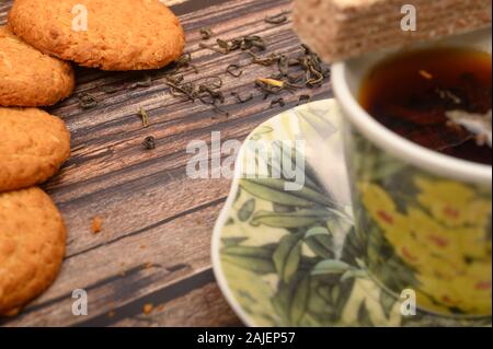 A Cup of black tea, tea leaves, pieces of brown sugar, oatmeal cookies, waffles on a wooden background. Close up Stock Photo