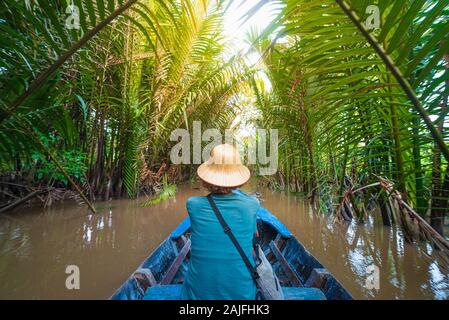 Boat tour in the Mekong River Delta region, Ben Tre, South Vietnam. Tourist with vietnamese hat on cruise in the water canals through coconut palm tre Stock Photo