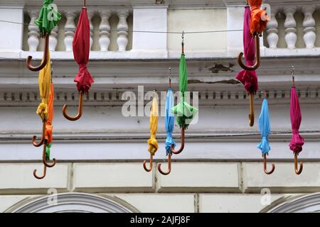 Many colorful closed umbrellas hanged outside on the street. Closed umbrellas up above the street. Stock Photo
