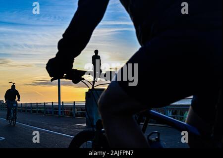 Brighton UK 4th January 2020 - Runners , walkers and cyclists enjoy a sunny but chilly morning along Brighton seafront as they pass by the statue of Olympic champion Steve Ovett at sunrise . Credit: Simon Dack / Alamy Live News Stock Photo
