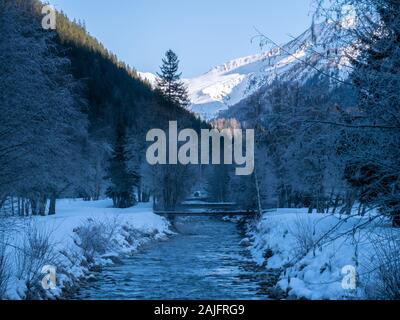A misty mountain stream flows through a snowy landscape. The trees and rocks are covered in snow to create a perfect winter tranquil scene. Stock Photo
