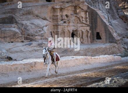 Petra, Jordan: Bedouin man riding a white horse nearby the archaeological area of the Treasury, UNESCO World Heritage Site Stock Photo