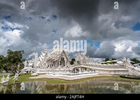 Chiang Rai, Thailand: Wat Rong Khun, White Temple, against a dramatic cloudy sky. This modern building is one of the main Thai attractions Stock Photo