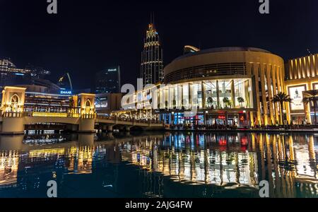Dubai, United Arab Emirates: Exterior of Dubai Mall by night opposite Burj Khalifa tower, illuminated shop windows, luxury fashion brands