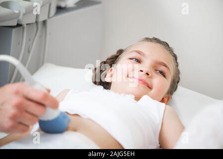 Medical exam of little girl by ultrasound equipment. Sonographer moving transducer on belly of child. Professional clinical diagnostics and treatment. Stock Photo