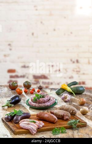 Selection of french raw sausage with arugula leaves in a wooden board,vegetable on the table on old white cracked red brick wall background. Stock Photo