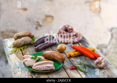 Selection of french raw sausage with arugula leaves in a wooden board,vegetable on the table on old white cracked wall background. Stock Photo
