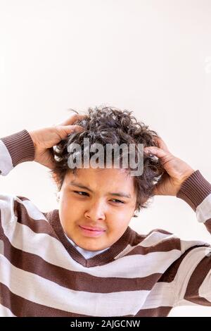 Boy scratching his head, looking annoyed on white background Stock Photo