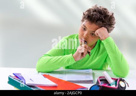 Nice boy at room: the boy has a pensive look and he sits at the table, doing homework Stock Photo