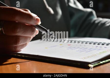 Woman writing in a bullet journal, low angle mid section view,  selective focus on pen nib. Stock Photo