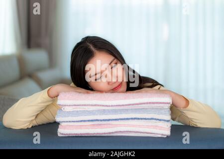 Happy Asian woman sleeping on clean folded clothes at home. Pretty young lady sitting in floor with sofa she dreamlike about something. Stock Photo