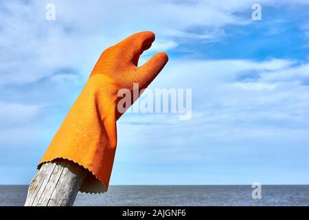 Rubber glove on wooden pole by the sea under a blue sky with clouds and copy space. Zero waste, plastic free, stop pollution, ecological concept. Stock Photo