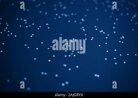 Glowing mica Silver stars confetti on blue color trendy background. Holiday confetti. Classic Flat lay. New Year 2020. Color of the year. Festive holi Stock Photo