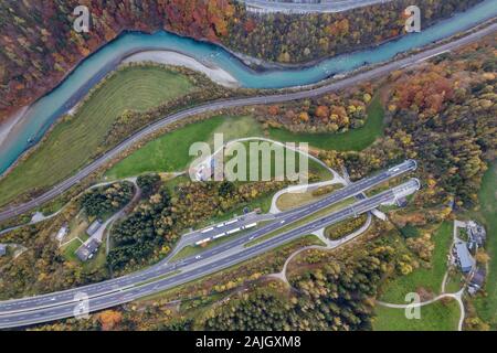 Top dawn aerial view of freeway speed road going out from undeground tunnel between yellow autumn forest trees and blue river. Stock Photo