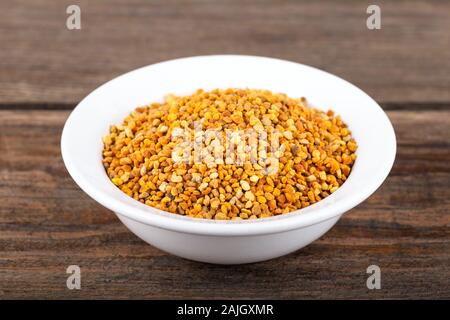 Bee pollen granules in white bowl on wooden background. Stock Photo