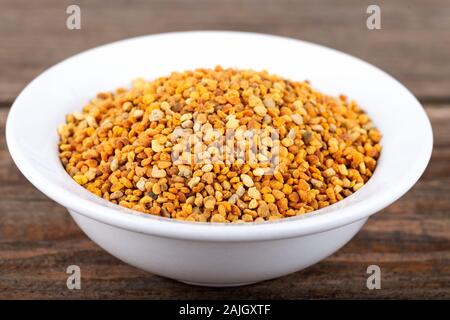 Bee pollen granules in white bowl on wooden background. Stock Photo