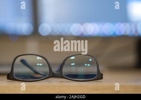 Closeup of protective glasses on an empty desk with blurred computer screen on background. Stock Photo