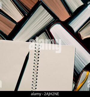 A black pencil with a notebook lie on the multicolored open books in the library Stock Photo