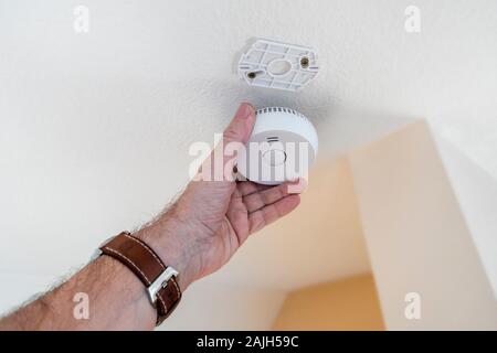Man fitting domestic smoke alarm / battery powered smoke detector on the ceiling in the hall at home Stock Photo