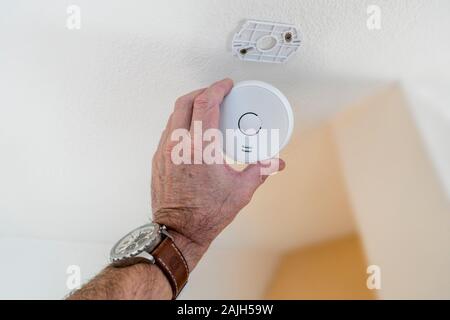 Man fitting domestic smoke alarm / battery powered smoke detector on the ceiling in the hall at home Stock Photo