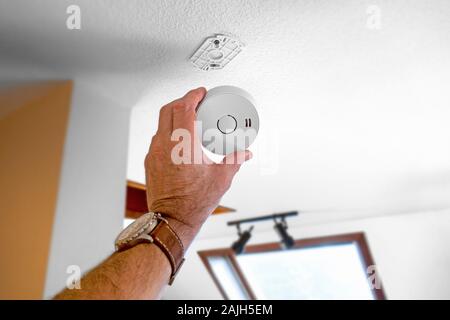 Man fitting domestic smoke alarm / battery powered smoke detector on the ceiling in the hall at home Stock Photo