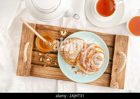 Sweet buns with walnuts, grated coconut and honey on a wooden tray. Breakfast concept. Top view, flat lay. Stock Photo