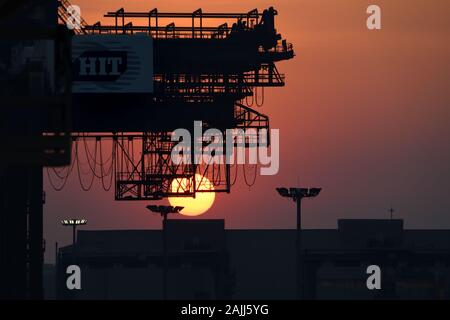 The sun setting behind the 'Hong Kong International Terminals' container crane at the Laem Chabang port in Thailand. Stock Photo