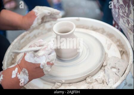 The potter makes pottery dishes on potter's wheel. The sculptor in workshop makes clay product closeup. Hands of the potter. Stock Photo