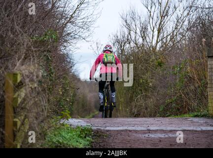 Female mountain bike cyclist on muddy railway path cycling route going over railway path bridge, East Lothian, Scotland, UK Stock Photo