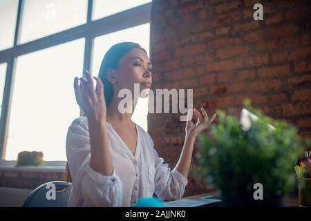 Beautiful calm young woman meditating at work Stock Photo