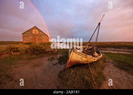 Boat wreck and boathouse at Thornham Old Harbour with rainbow at sunrise, Thornham, Norfolk, England, United Kingdom, Europe Stock Photo