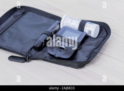 Glucometer, lanset and test strip lies in bag case on the wooden table on the left side. Concept of health, medicine. Stock Photo