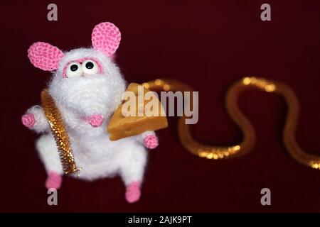 White knitted toy rat with piece of cheese on dark red background, New Year card with golden decoration. Chinese Year of Rat, Zodiac symbol 2020 Stock Photo