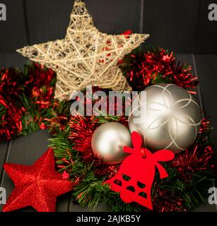 Christmas decoration with gold star and silver balls on red and green tinsel, red velvet bell and star with bright and red glitter with dark wooden ba Stock Photo