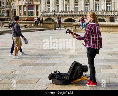 Young female musician, guitar player and singer performs for people in the large square outside of Cologne Cathedral in Germany. Stock Photo