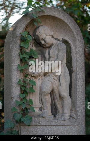 Statue of a cherub on a tombstone overgrowing with ivy Stock Photo