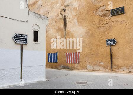 Scenery of Fes (Fez) in Morocco with signposts showing the way to the popular tourist attractions and some interesting fabrics on the wall Stock Photo