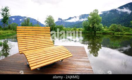 Oversized wooden deck chair on pretty pond reflecting the misty mountains around Oberammergau, Germany, famous for the Passion Play. Stock Photo